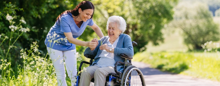 Life Assure Senior Woman In Wheelchair With Caregiver At Park Hero